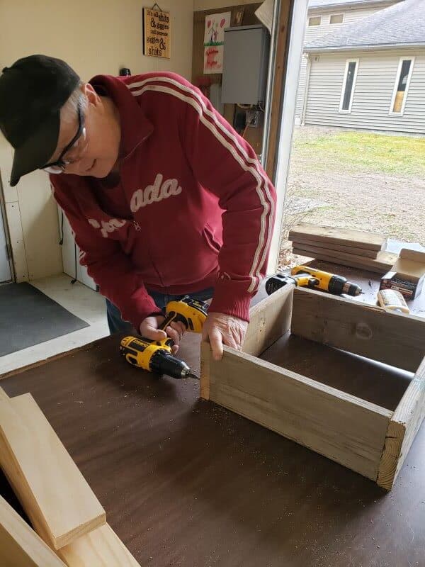 homme assemblant une boîte de jeu de lancer de rondelles avec une perceuse manuelle